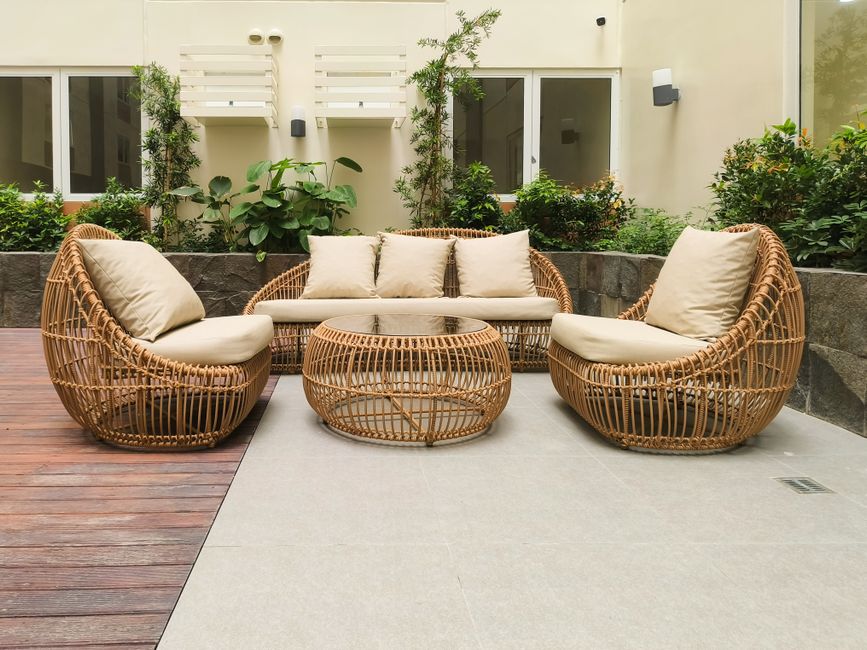 Rotan ligstoel met groene planten op achtergrond.